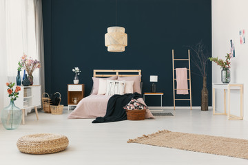 Real photo of elegant hotel room interior with dark blue wall, double bed with powder pink bedclothes and fresh flowers in vases