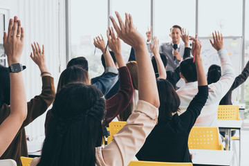 Audience raising hands up while businessman is speaking in training at the office.