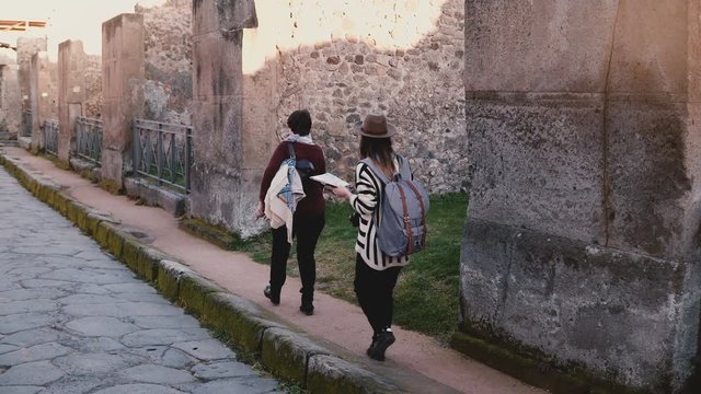 Camera follows two women with a map walking along old antique ruins and streets of Pompeii, Italy on travel vacation.