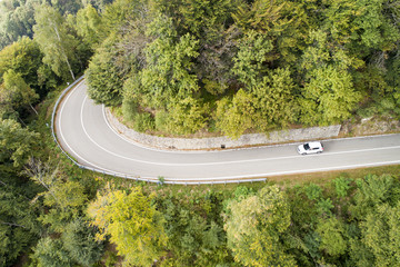 Mountain road in the woods with passing car. Aerial view.