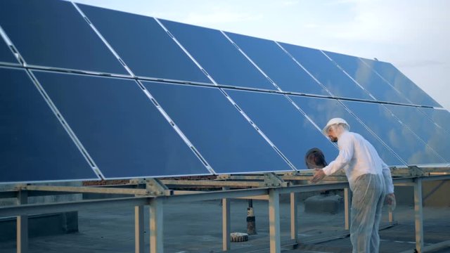 Male specialist in protection clothes is cleaning a solar panel. Alternative energy concept.