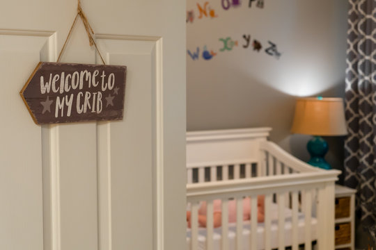 Baby Sleeping In A Crib.  The Door To The Nursery Has A Welcome To My Crib Sign.  Peaceful Baby Sleeping In The Background