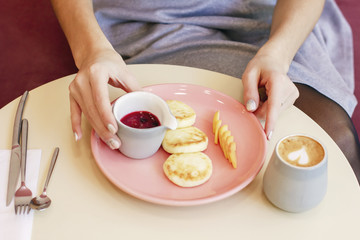 The young woman has Breakfast in cafe cheesecakes with berry jam and coffee