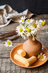 Still life of a bouquet of daisies in a vase and waffle tubes. Wooden rustic style.