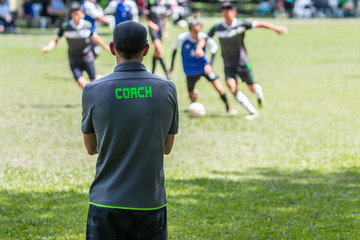 Male soccer or football coach standing on the sideline watching his team play