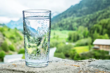 Fototapete Wasser Glas Wasser auf dem Stein. Unscharfe Schneeberggipfel und grüne Wälder im Hintergrund.