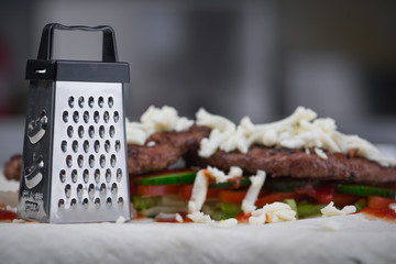 A small grater stands next to a meat roll, a cutlet, cheese and vegetables. Маленькая терка стоит рядом с мясным ролом, котлета, сыр и овощи.