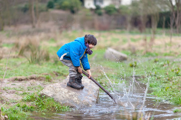 Boy splashing water with stick in creek