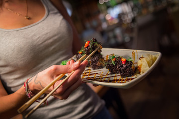 A girl in a restaurant holds a plate of sushi rolls in her hands and eats. Девушка в ресторане держит в руках тарелку с суши ролами и ест.