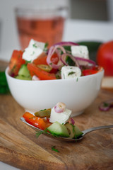 Greek salad lies on a spoon in the background of the dish. Греческий салат лежит на ложке на фоне блюда.