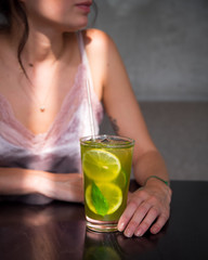 the girl is sitting at a table in a restaurant on the table is a cocktail on it falls a glare of light. девушка сидит за столом в ресторане на столе стоит коктейль на него падает блик света.