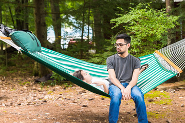 A young man is listening to hhis younger sister laying in a green hammock