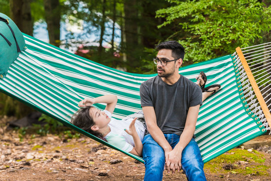 A young girl is talking to her older brother in a green hammock