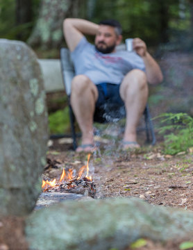 A blurried man is drinking as a background of a burning camp fire