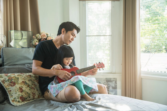 Beautiful little girl playing guitar with her father. Happy lifestyle picture. Happy family timespending. Girl holding red ukulele ang singing.