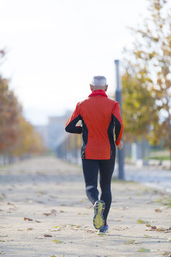 A senior man dressed in black and orange is running in the park