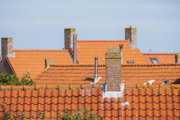 stone chimneys on the roofs with orange roof tiles against a blue sky in an old neighborhood