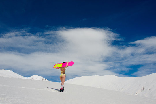 Rear view of young sexy girl with a snowboard on her shoulders