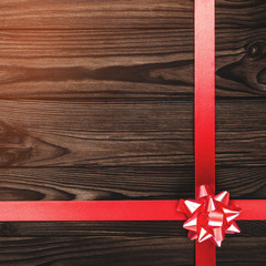 Fototapeta premium View from above of a Merry Christmas inscription on dark brown wooden background with red ribbon, greeting card with space for text writing, with light bulbs