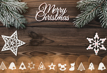 View from above of a Merry Christmas inscription and handmade tree toys, stars and evergreen branch on wooden background, greeting card with space for text writing, with light bulbs