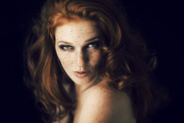 Beautiful young woman with red hair and freckles portrait, beauty shoot on dark background,...