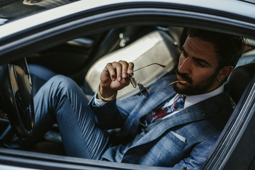 Entrepreneur sitting in the car and holding his sunglasses