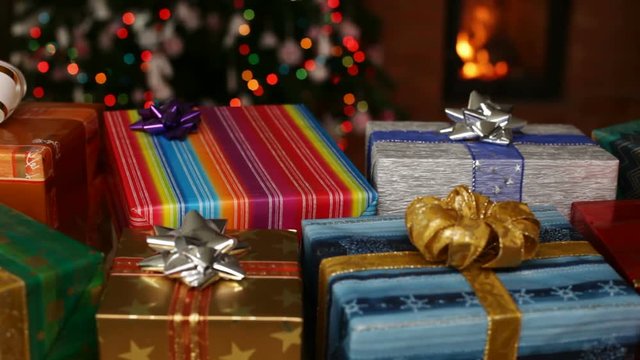 Many christmas gifts in front of fireplace and blurry lights on xmas tree in the evening - camera sliding slow, closeup