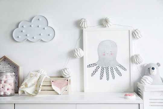 Stylish scandinavian newborn baby room with toys, teddy bears, wooden boxes and cloud. Modern interior with mock up photo frame and childs accessories.
