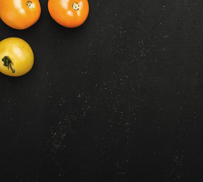 Three juicy tomatoes at the top of the image on black textured background. Fresh vegetables for consumption, top view