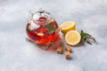 Glass teapot with tea, mint and lemon on grey table with copy space