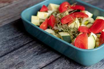 Zucchini, tomatoes and capers in a blue baking dish on wood background