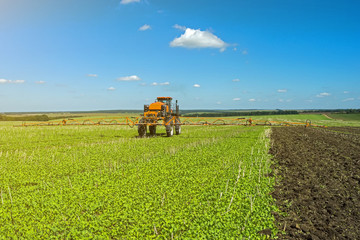 self-propelled sprayer works on a field under a blue sky with clouds