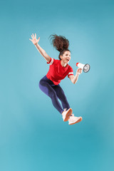 Beautiful young woman jumping with megaphone isolated over red background. Runnin girl in motion or...