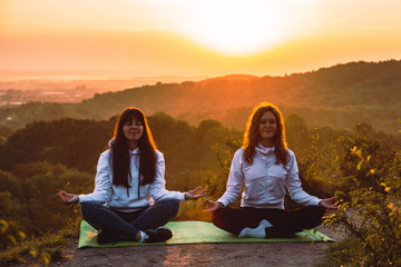 couple of women sitting at the edge of the hill. do yoga exercises on sunrise