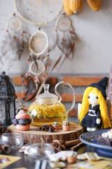 Halloween witchcraft party with herbal afternoon tea and macaron dessert in wicca and pegan concept with tarot cards. Selective focus on the  Chrysanthemum tea. Cute crochet witch doll.