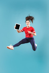 Gadget in modern life. Jump of young woman over pink studio background using laptop or tablet gadget while jumping. Runnin surprised girl in motion or movement. Human emotions and facial expressions