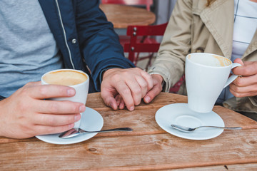 couple holding hands while drinking latte in outdoors cafe