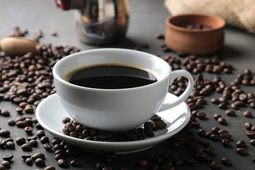 Coffee in a white cup close-up and roasted coffee beans around on a black background.