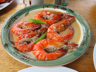 The plate of appetizing tiger shrimps. Five red cooked shrimps with gravy and green leafs.