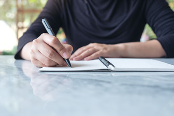 Closeup image of business woman writing on blank notebook on table with green nature background