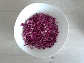 Bowl with sliced red cabbage on a white wooden background