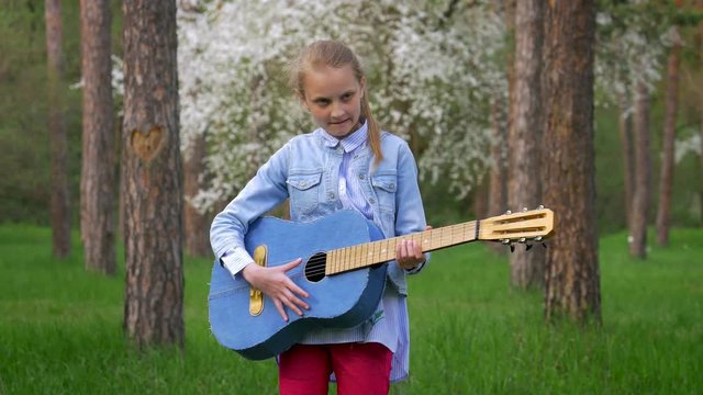 Caucasian little girl female playing guitar in a park