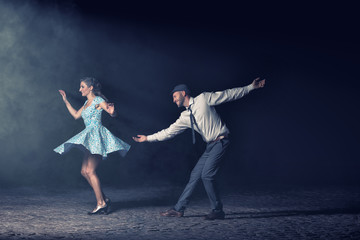 Couple dancing lindy hop at night in front of a spotlight.