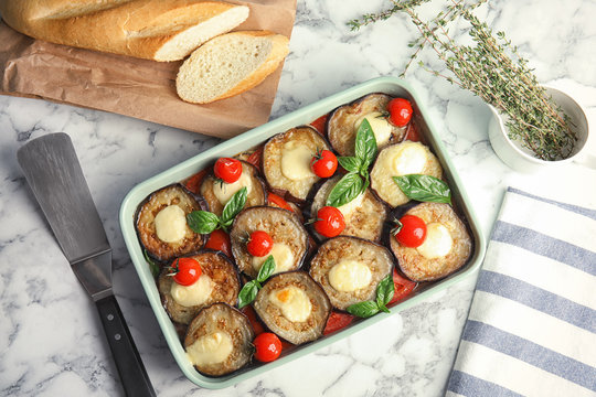 Flat lay composition with baked eggplant, tomatoes and basil in dishware  on marble table