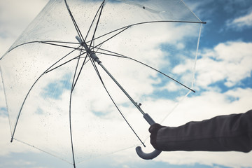 Female hand with a transparent umbrella on a rainy autumn day on the cloudy sky background