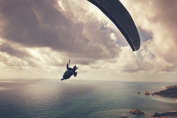Silhouette of a man flying on a paraglider  high above the sea in the clouds, sport, beauty and freedom concept