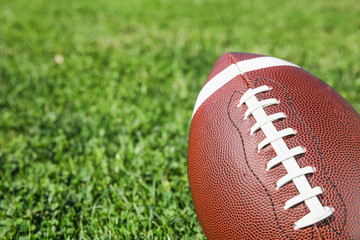 Ball for American football on fresh green field grass, closeup. Space for text