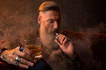 Portrait eines attraktiven Geschäftsmannes mit einer Zigarre und einem Glas Whiskey vor dunklem...