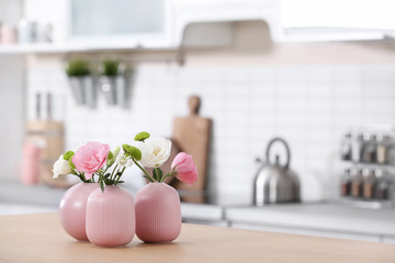 Vases with beautiful flowers on table in kitchen interior. Space for text