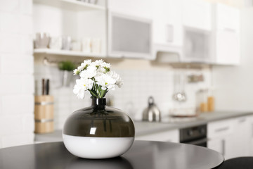 Vase with beautiful flowers on table in kitchen interior. Space for text